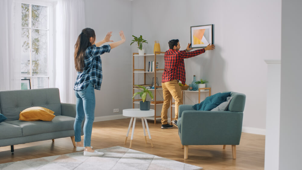 couple décorant son salon en accrochant un cadre au mur