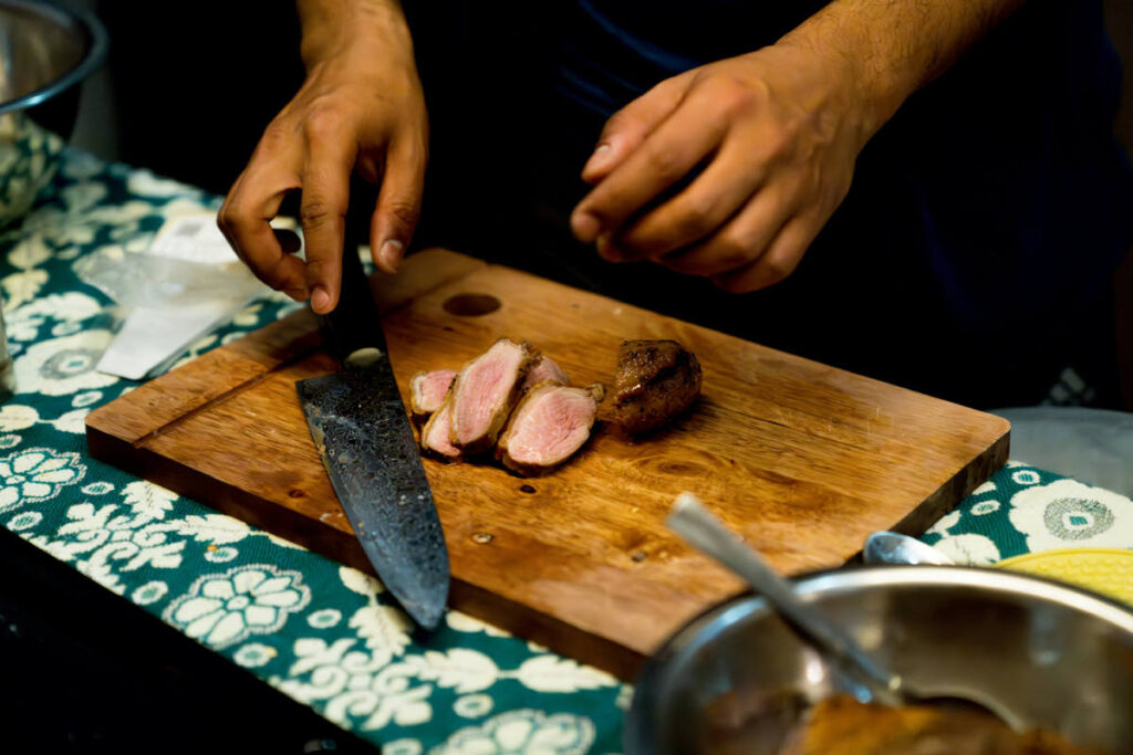 Magret de canard laqué et brillant découpé en tranches sur une planche en bois
